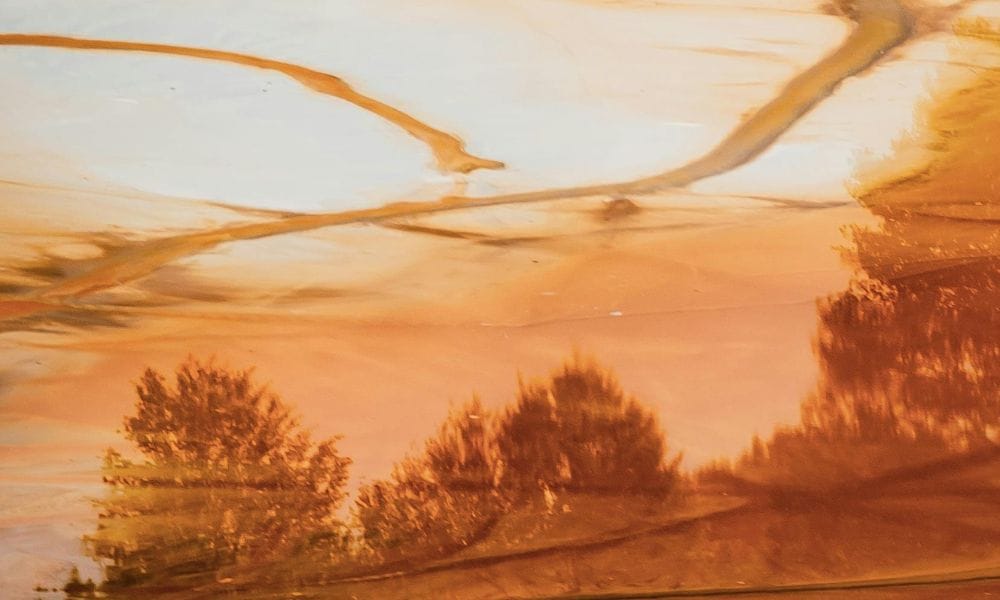The image is of an orange toned underpainting featuring a loose soft composition of the sky and trees. The trees are of a reddish brown shade while the sky is of a light orange shade. Landscape painting.